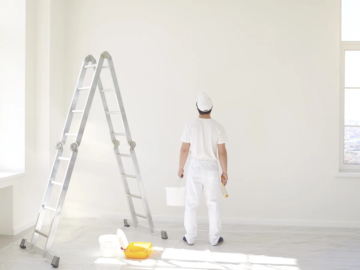 Painter on ladder rolling paint on exterior window frames in Wilmslow