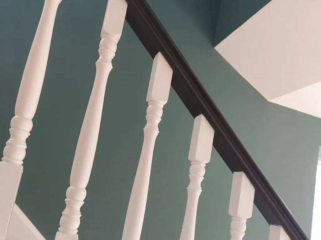 White staircase spindles and dark handrail against teal walls, painted by Cheshire Painters.